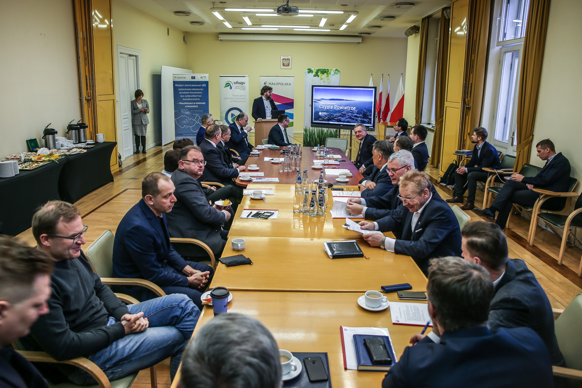 osoby siedzą przy stole, jedna osoba przemawia