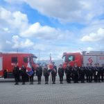 Zdjęcie jednostki osp na tle samochodów strażackich podczas wręczenia promes.