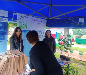 Zdjęcie przedstawia stoisko informacyjne, w namiocie wystawienniczym, w którym znajdują się trzy kobiety.